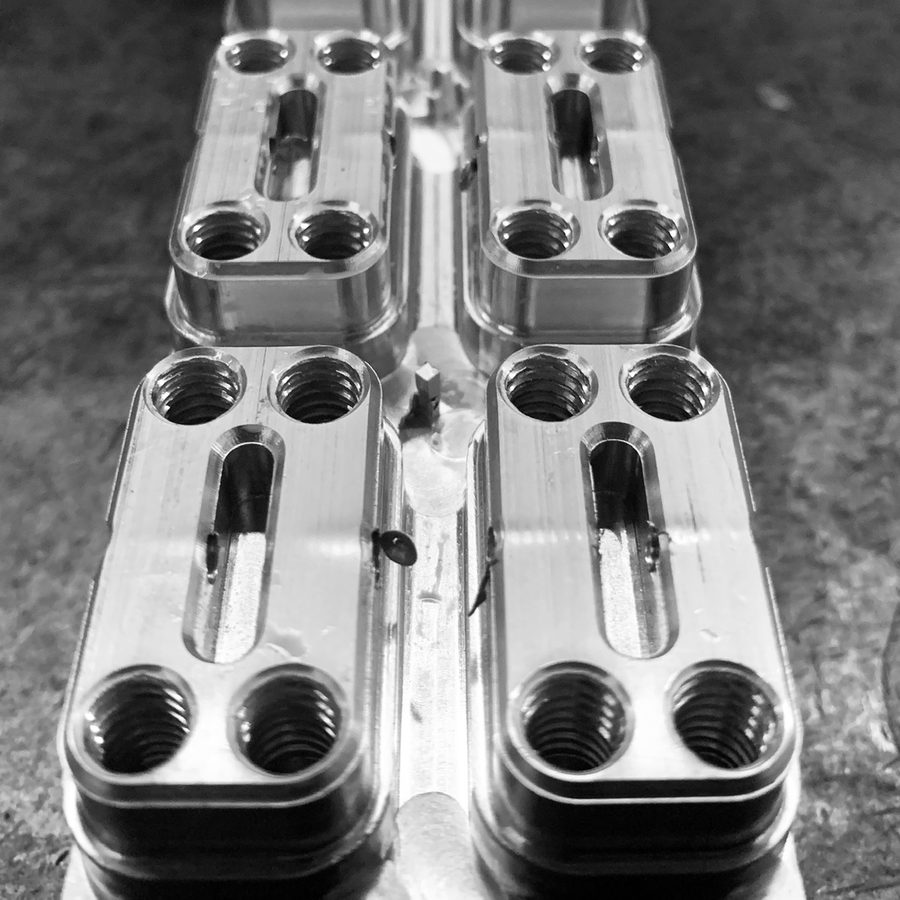 A row of machined aluminum blocks with threaded ports and slots, viewed lengthwise